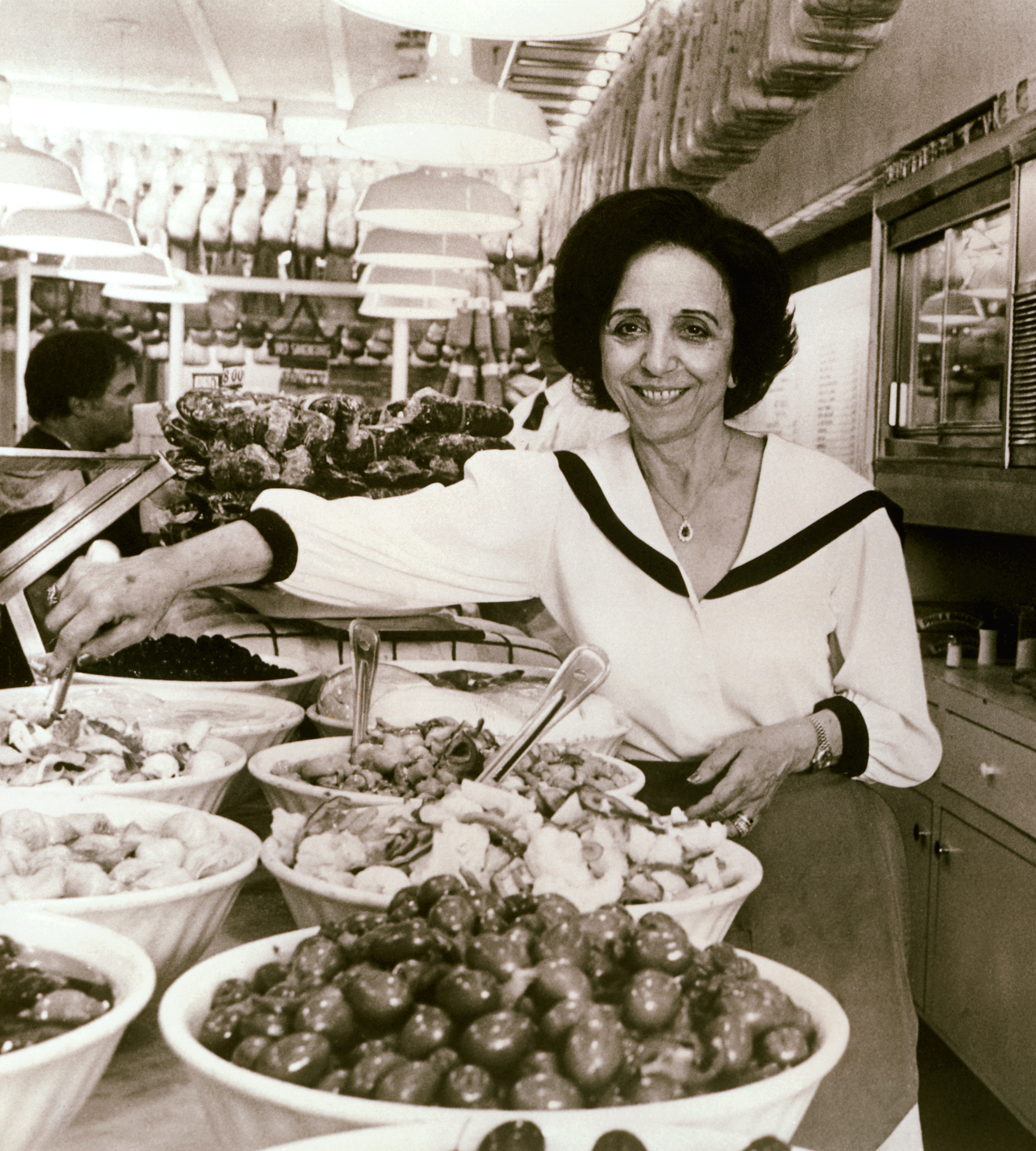 ‘Mama’ Carmela Sbarro, a tall Italian woman with short, dark hair, stands in line with eight Italian dishes prepared at the original Sbarro